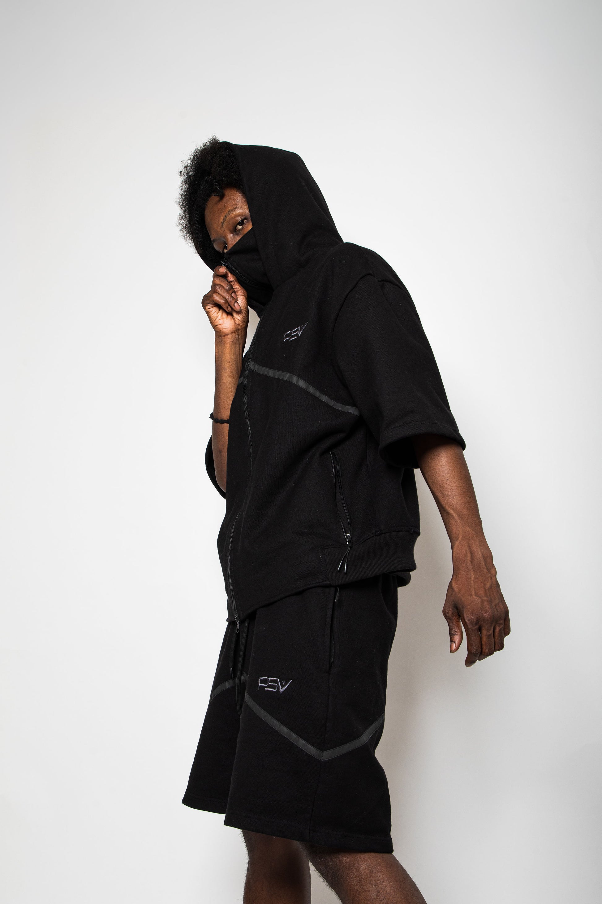 Person wearing a black hoodie and shorts with a brand logo on a white background
